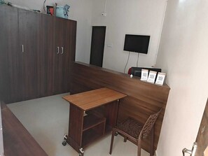 Une petite pièce privée comprenant un bureau, une chaise, une armoire et un téléviseur à écran plat fixé au mur.