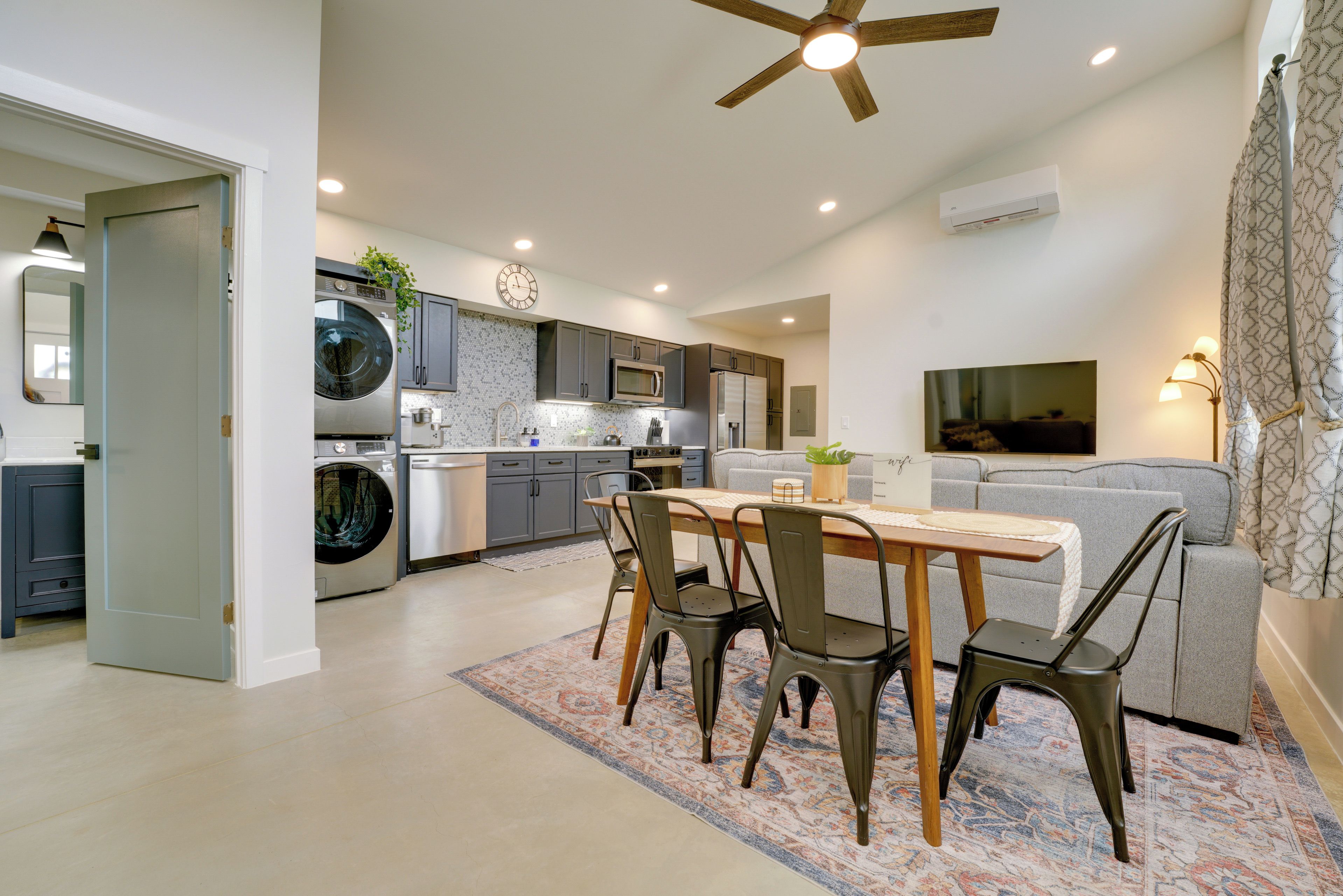 A modern kitchen with a dining area, a ceiling fan, and a living room with a sofa and a TV.