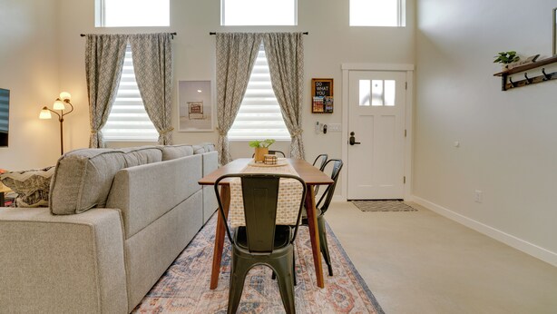 Una sala de estar con un sofá, una mesa de comedor con sillas, un ventilador de techo y una puerta con un perchero encima.