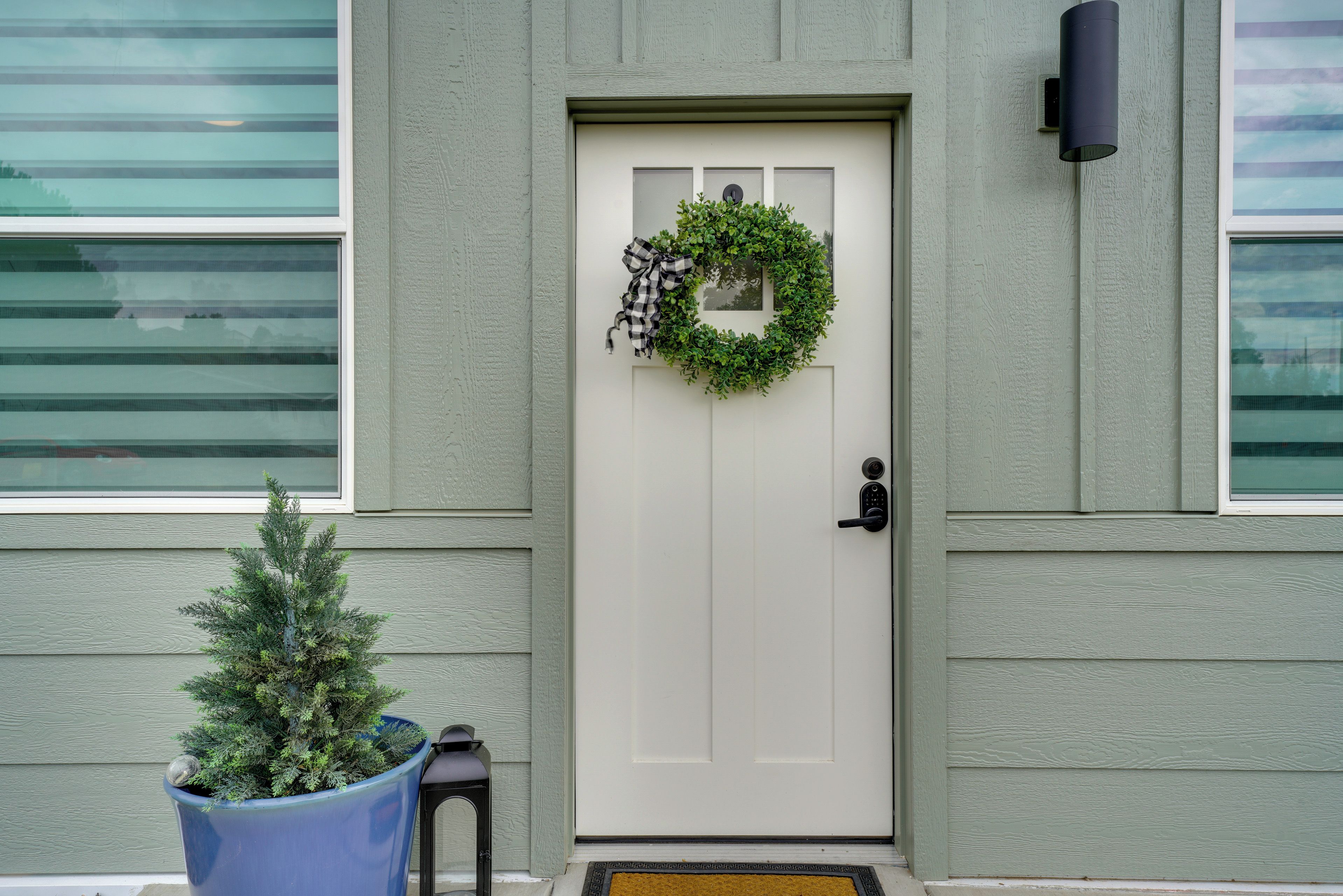 A front door with a wreath, a potted plant, and a doorbell.