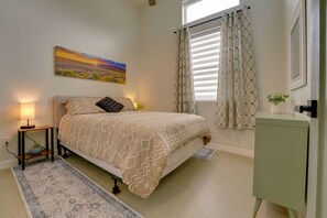 A bedroom with a bed, bedside lamp, a painting on the wall, a window with curtains, and a small cabinet. - Modern Unit Near the Best of Grand Junction (Grand Junction)