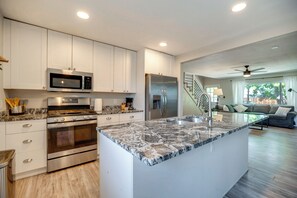 A modern kitchen with stainless steel appliances, a marble countertop, and a view to a living area with a staircase. - Mountain-view Basecamp in Central Colorado Springs (Colorado Springs)