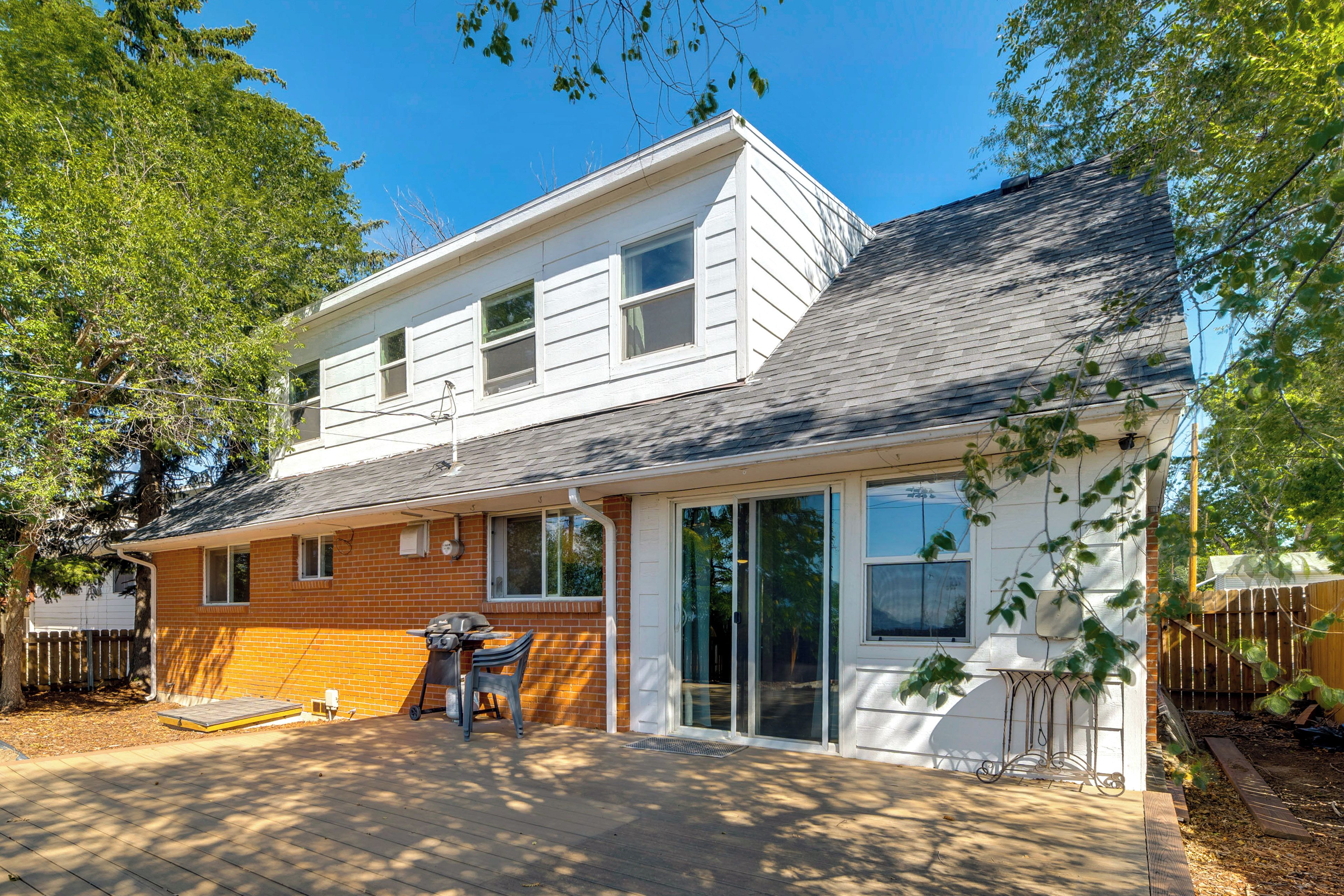 Ein zweistöckiges Haus mit überdachter Terrasse, Backsteinelementen und einer Holzterrasse.