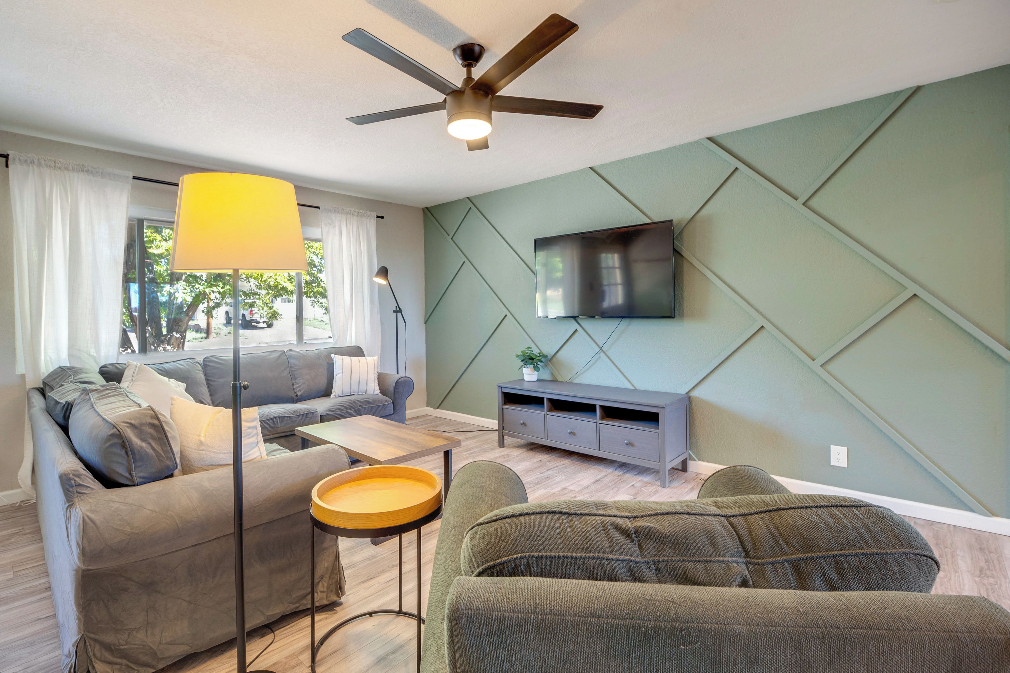 A modern living room with a sofa, a coffee table, a floor lamp, a TV mounted on the wall, and a ceiling fan.