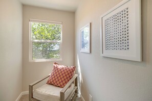 Een hoekappartement met raam, een stoel met een patroonkussen, en twee ingelijste kunstwerken aan de muur.
