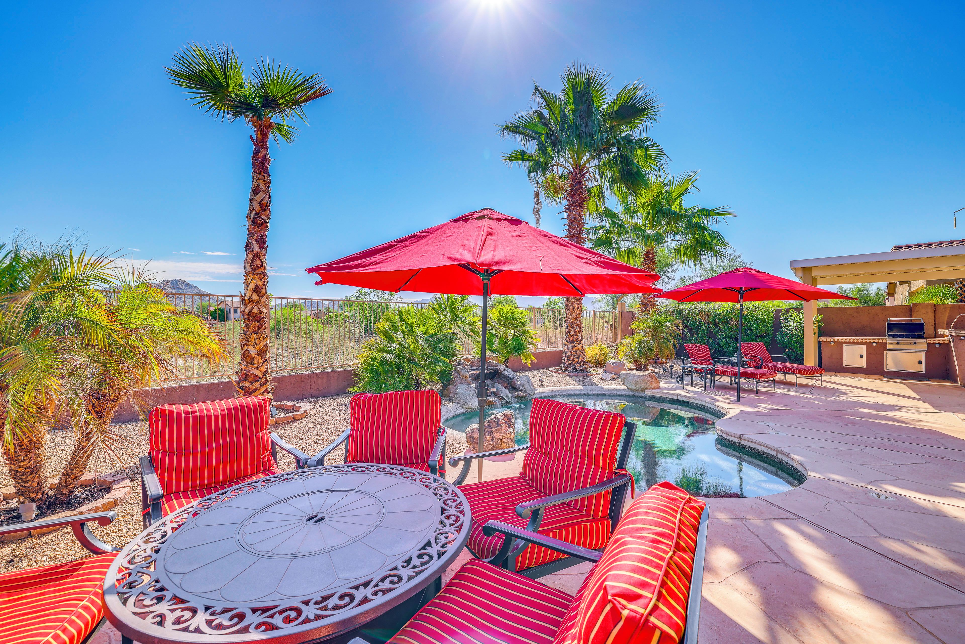 A poolside area with red-striped chairs, a round table, and red umbrellas.