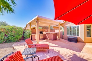 Eine Außenpatio mit Grillplatz, rot gestreiften Stühlen und einem roten Sonnenschirm.