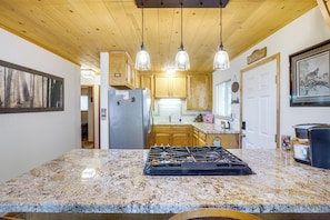 A kitchen with granite countertops, a gas stove, wooden cabinets, and pendant lighting. - Calaveras Adventure Lodge in Blue Lake Springs (Arnold)