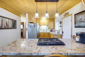 Una cocina con encimeras de granito, estufa a gas, armarios de madera e iluminación colgante.