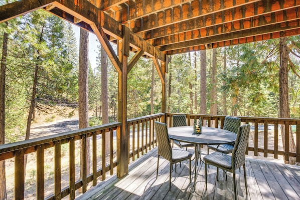 A wooden deck with a table and chairs, surrounded by trees. - Calaveras Adventure Lodge in Blue Lake Springs (Arnold)
