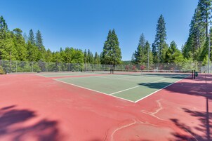 Cancha de tenis con superficie roja, rodeada de una valla y árboles.