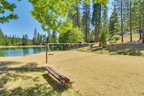 A sandy beach volleyball court with a bench, surrounded by tall trees and a lake. - Calaveras Adventure Lodge in Blue Lake Springs (Arnold)