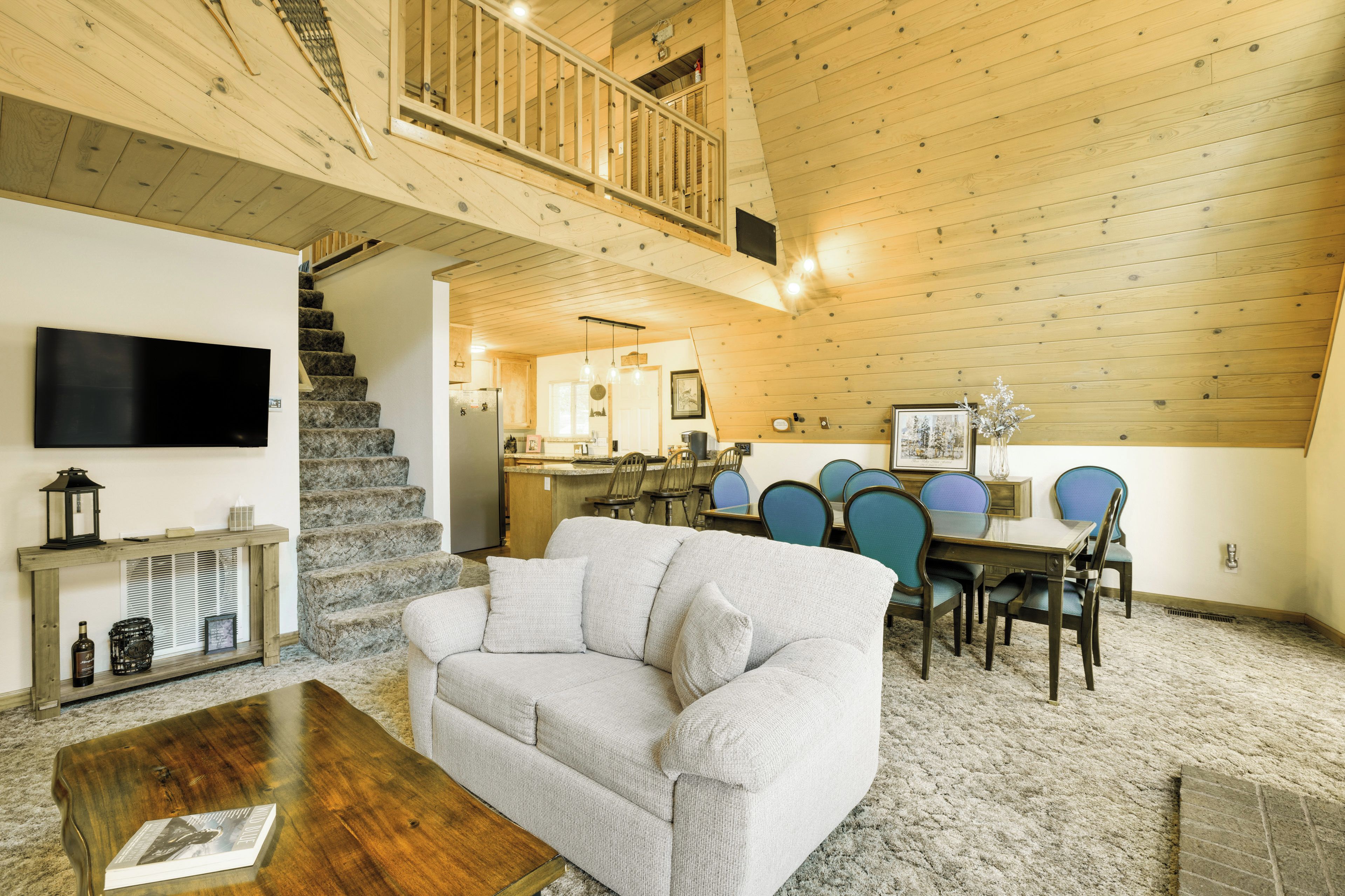 A spacious living area with a sofa, coffee table, and a dining table with chairs. A staircase leads to an upper level.