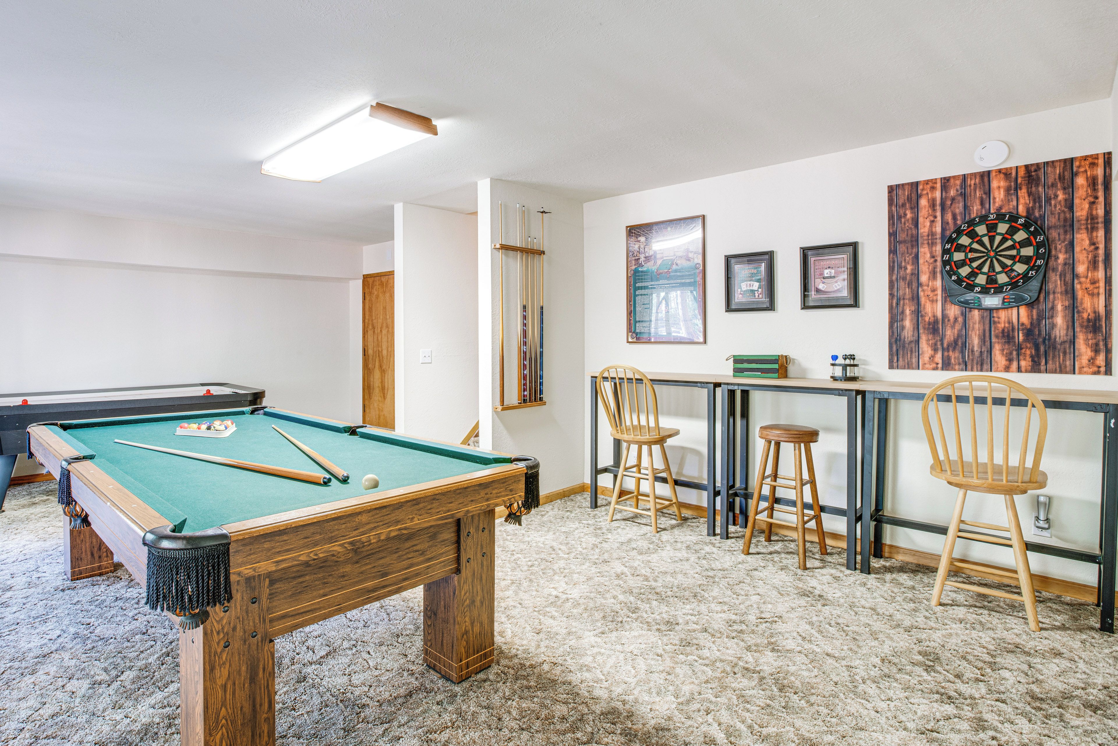 A room with a pool table, a dartboard, and a bar area with stools.