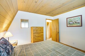 A bedroom with a bed, a dresser, a nightstand, a lamp, a framed picture, and a door leading to another room. - Calaveras Adventure Lodge in Blue Lake Springs (Arnold)