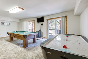 Una habitación con mesa de billar, mesa de hockey de aire y televisor montado en la pared.