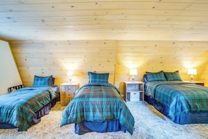 Una habitación con tres camas alineadas, paredes de madera y dos mesitas de noche con lámparas.