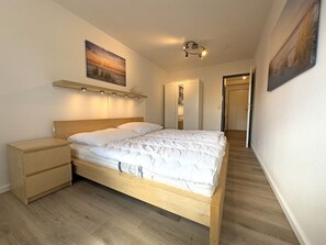 A bedroom with a wooden bed, a nightstand, a bedside table, and a wall-mounted shelf. - Holiday Apartment With 2 Bedrooms (Varel)