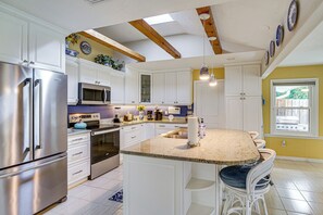 A kitchen with white cabinetry, stainless steel appliances, and a breakfast bar with white chairs.