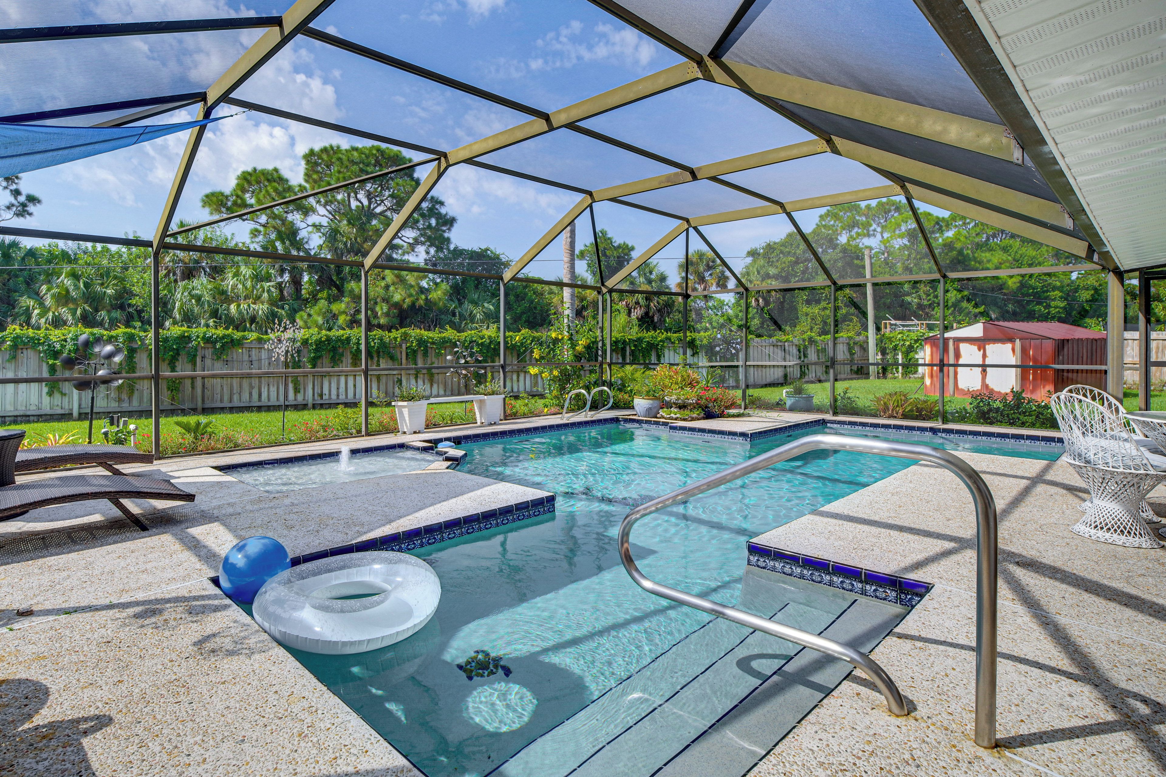 A covered outdoor swimming pool with a clear view of the surrounding greenery and a wooden fence.