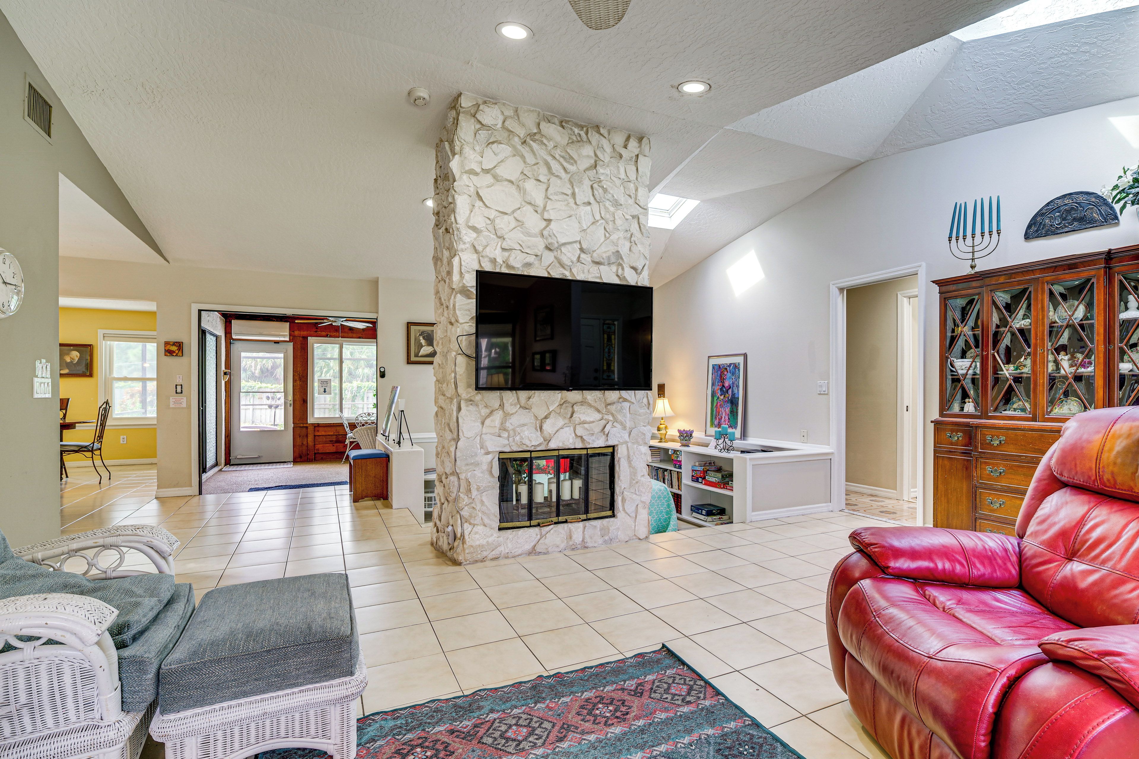 A living room with a stone fireplace, a television mounted on the wall, a red leather sofa, and a dining area in the background.