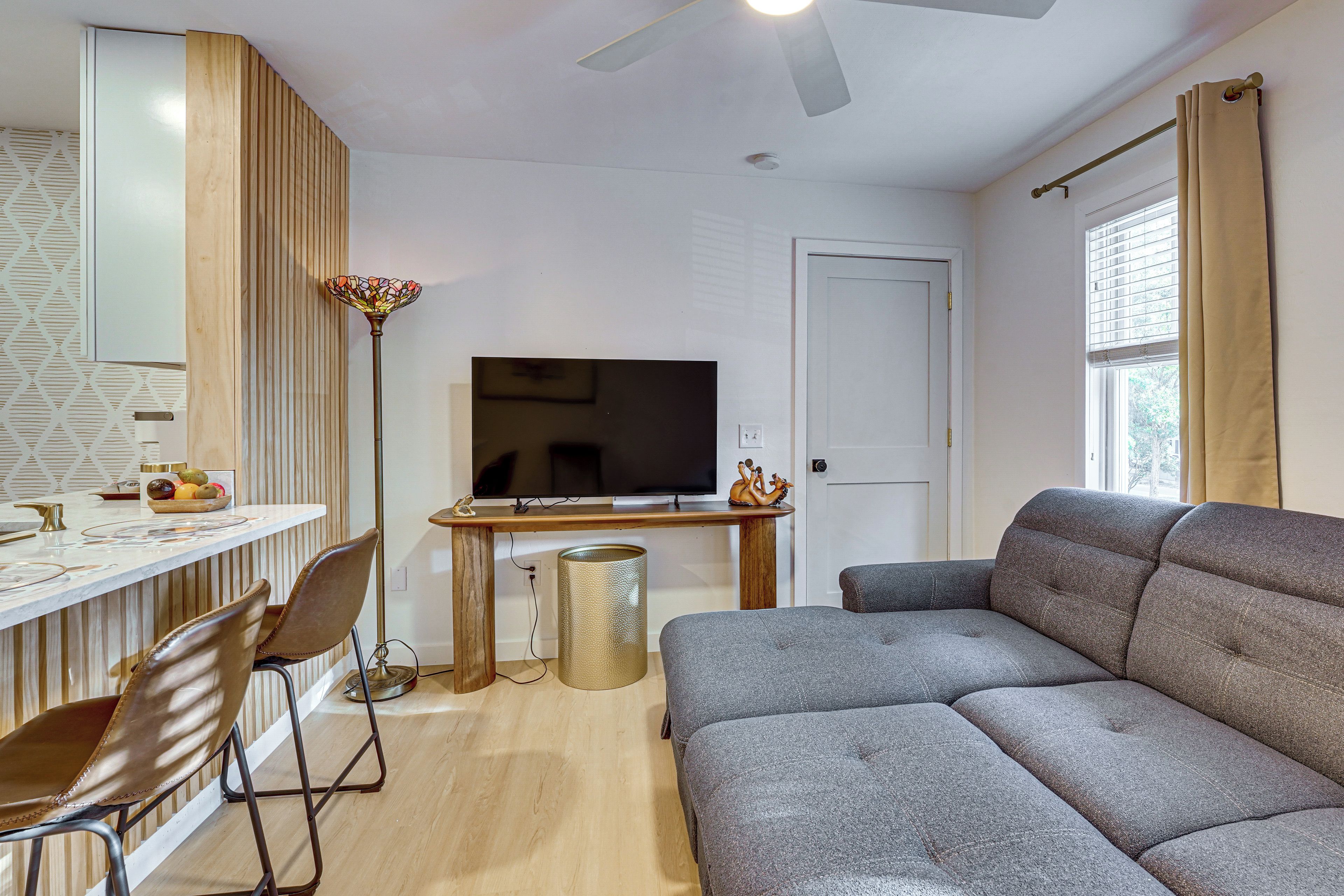 En moderne stue med sofa, fjernsyn, spiseplads med stole og en dekorativ gulvlampe.