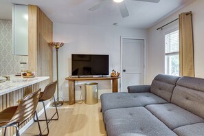 A modern living room with a sofa, a television, a dining area with chairs, and a decorative floor lamp.