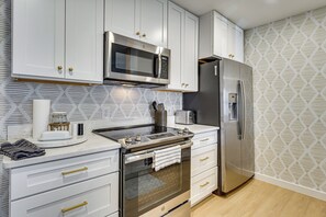 A modern kitchen with white cabinets, a stainless steel oven, a microwave, and a refrigerator. - Haile Village Center: Near UF Dining, Shops 2 Blks (Gainesville)
