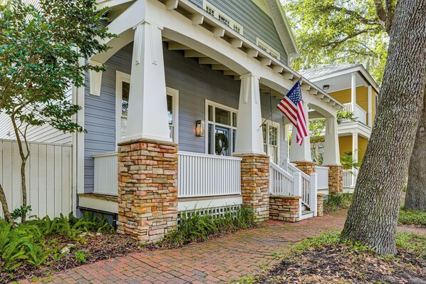 A two-story house with a porch, stone pillars, and an American flag.