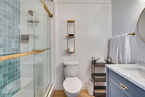 Un baño moderno con cabina de ducha de vidrio, inodoro, lavamanos de mármol y toallero.