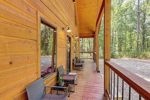 Una cabaña de madera con porche cubierto, mobiliario exterior y vistas a un bosque.