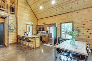 Interior de una cabaña de madera con cocina, comedor y asientos de bar.