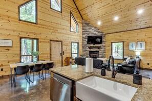 A spacious kitchen with a large island, a dining area with chairs, and a fireplace. - Private Hot Tub + Fire Pit: Broken Bow Escape (Broken Bow)