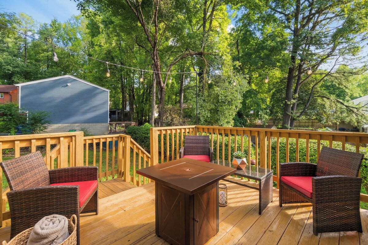 A wooden deck with wicker furniture and a table, surrounded by trees.