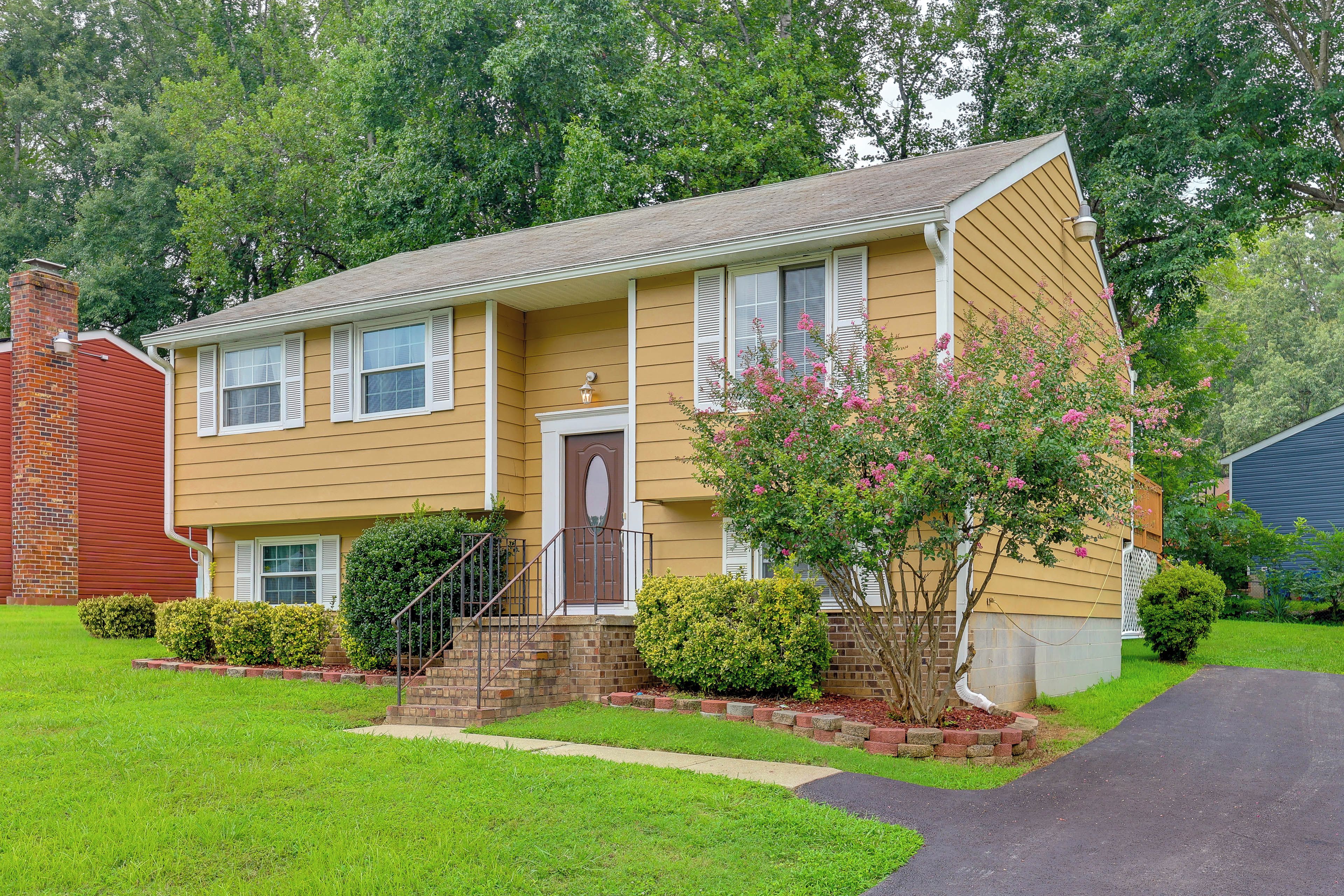 A two-story residential house with a front porch, a brick chimney, and a well-maintained lawn.