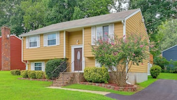 A two-story residential house with a front porch, a brick chimney, and a well-maintained lawn.