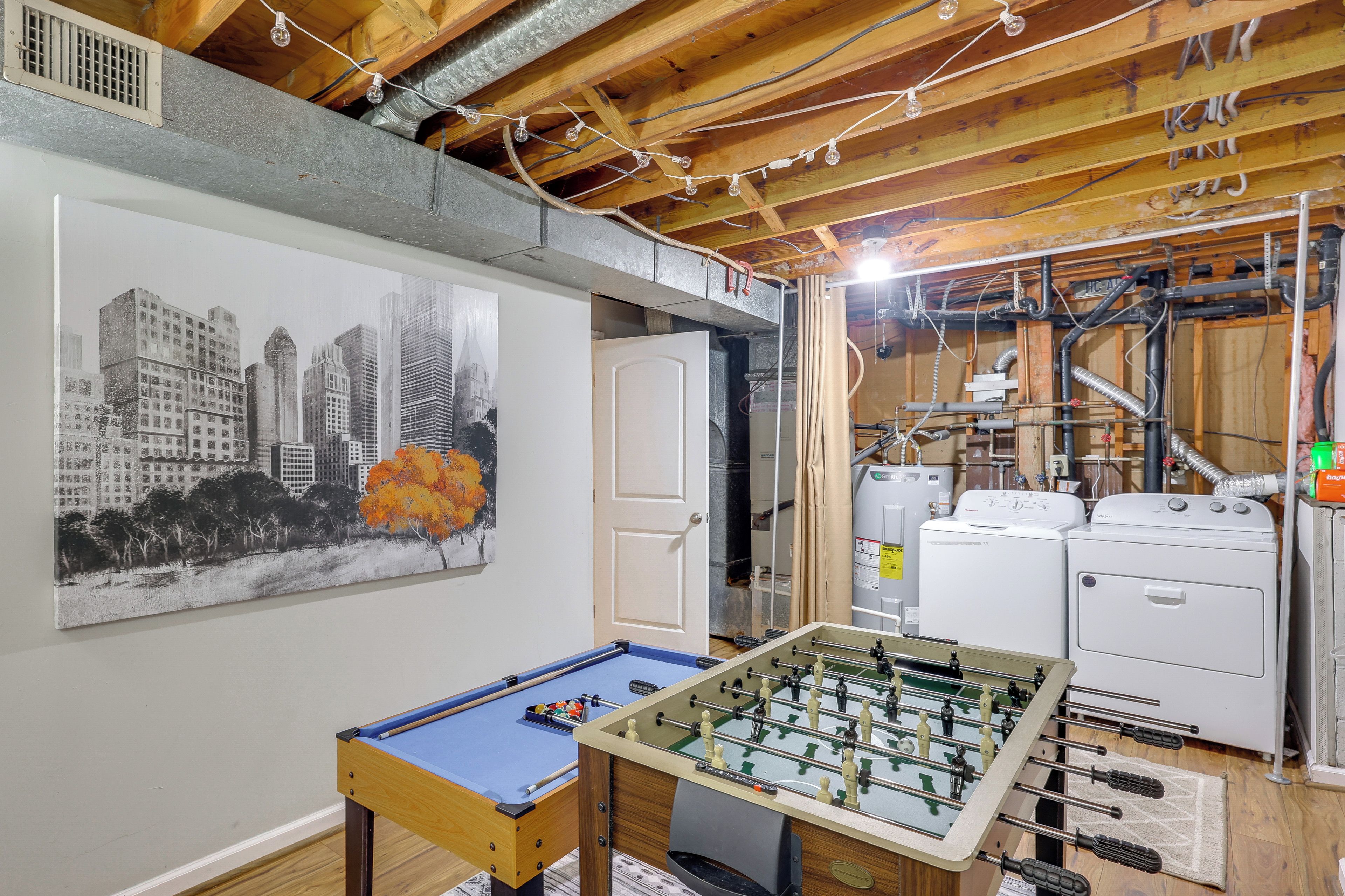 A room with a foosball table, a painting of a cityscape, and a kitchen area with appliances.