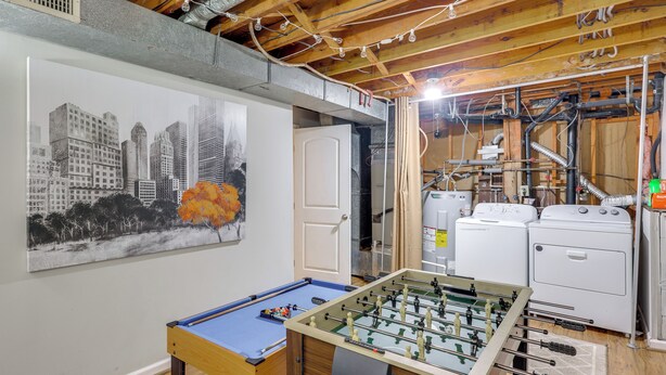 A room with a foosball table, a painting of a cityscape, and a kitchen area with appliances. - Charming Family Home 11 Mi to Dtwn Richmond! (Chesterfield)