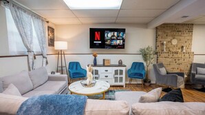 A living room with a sofa, two armchairs, a coffee table, a TV mounted on the wall, and a brick wall. - Charming Family Home 11 Mi to Dtwn Richmond! (Chesterfield)