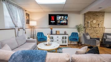 A living room with a sofa, two armchairs, a coffee table, a TV mounted on the wall, and a brick wall.