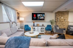 A living room with a sofa, two armchairs, a coffee table, a TV mounted on the wall, and a brick wall.