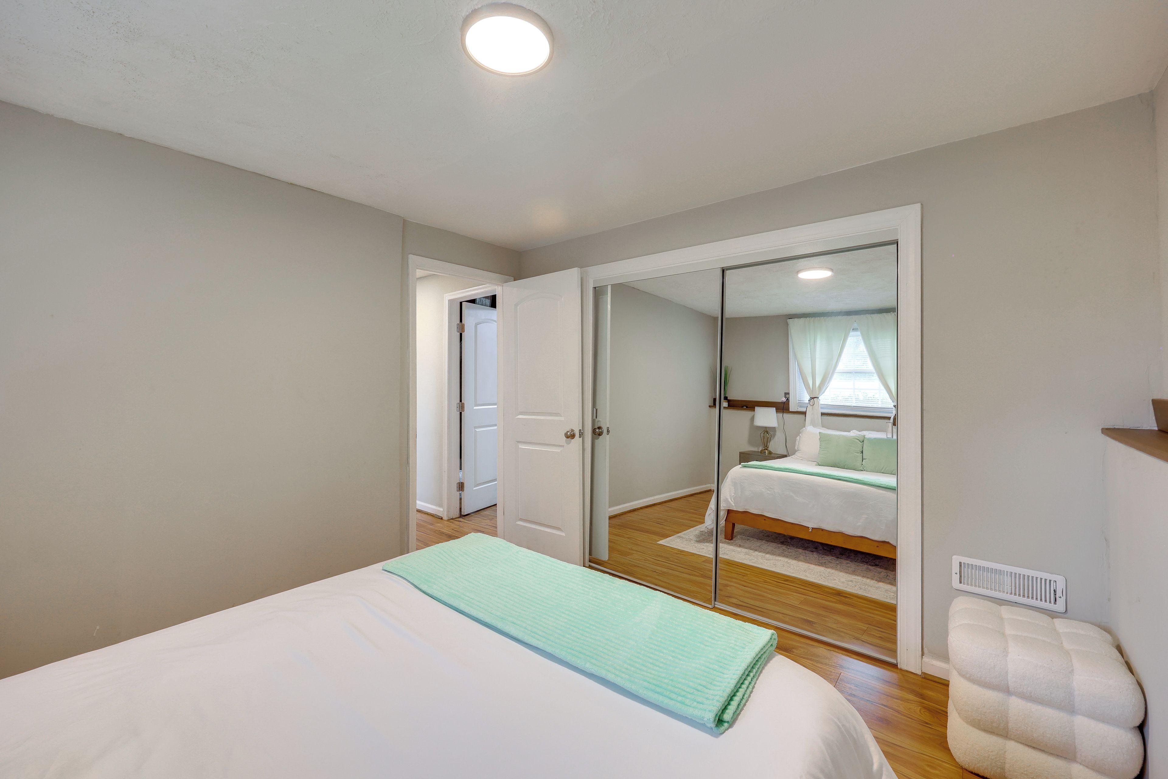 A bedroom with a bed, a bedside table, a mirror, and a door leading to another room.