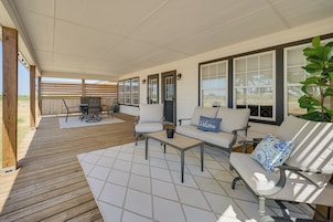 A covered patio area with a wooden deck, outdoor furniture, and large windows.
