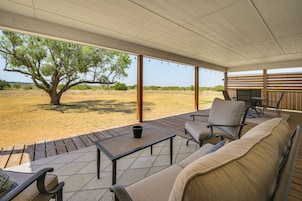Un área de estar al aire libre con mesa, sillas y sofá, con vistas a un paisaje natural con árboles y campos abiertos.