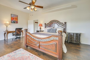 A bedroom with a wooden four-poster bed, a ceiling fan, a nightstand, a desk, and a chair.