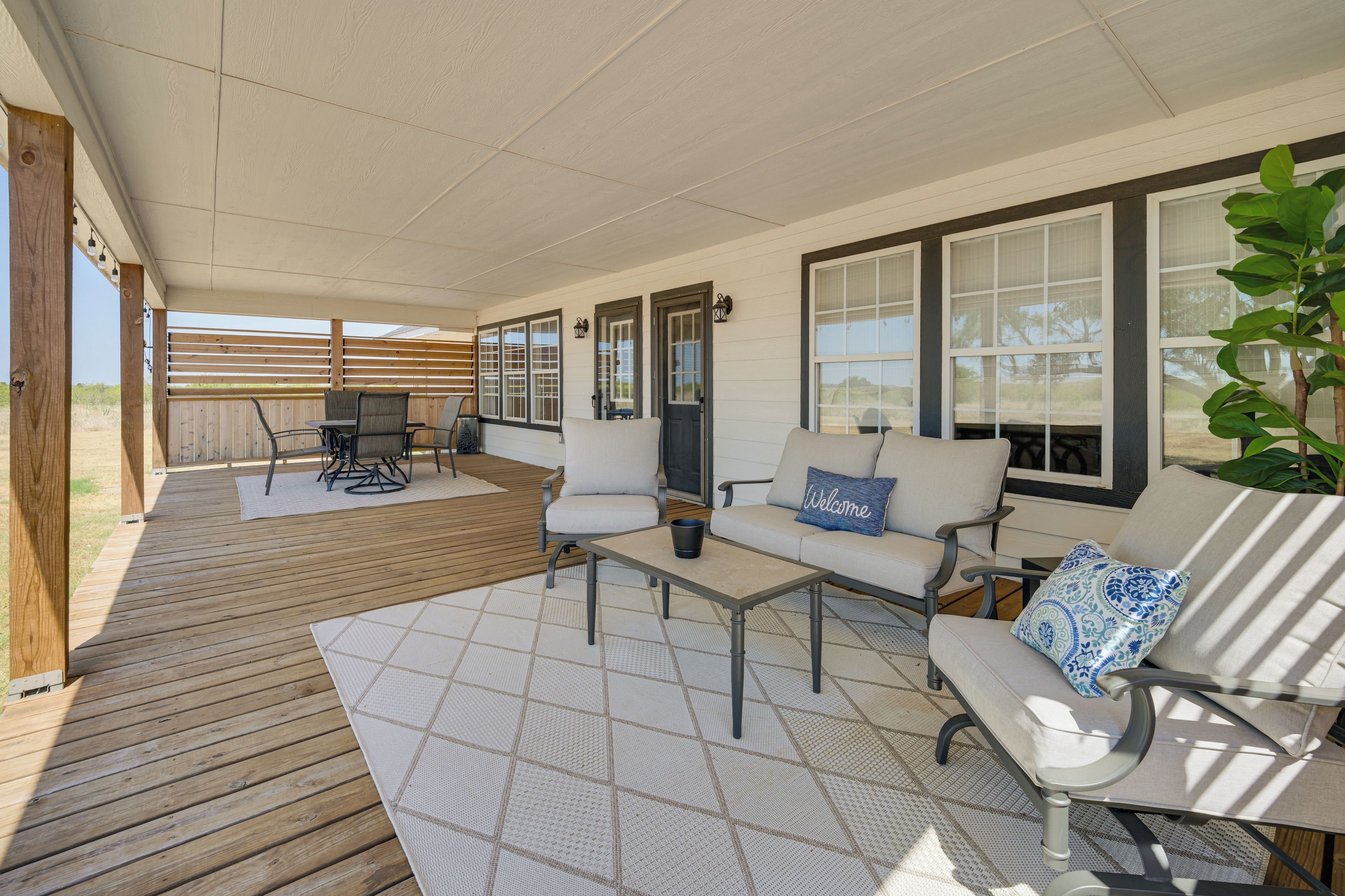 A covered patio area with a wooden deck, outdoor furniture, and large windows.