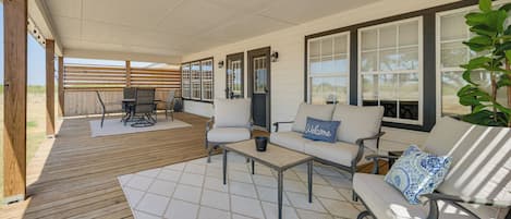 A covered patio area with a wooden deck, outdoor furniture, and large windows.