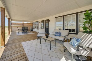 Uma área de pátio coberta com deck de madeira, mobiliário de exterior e grandes janelas.