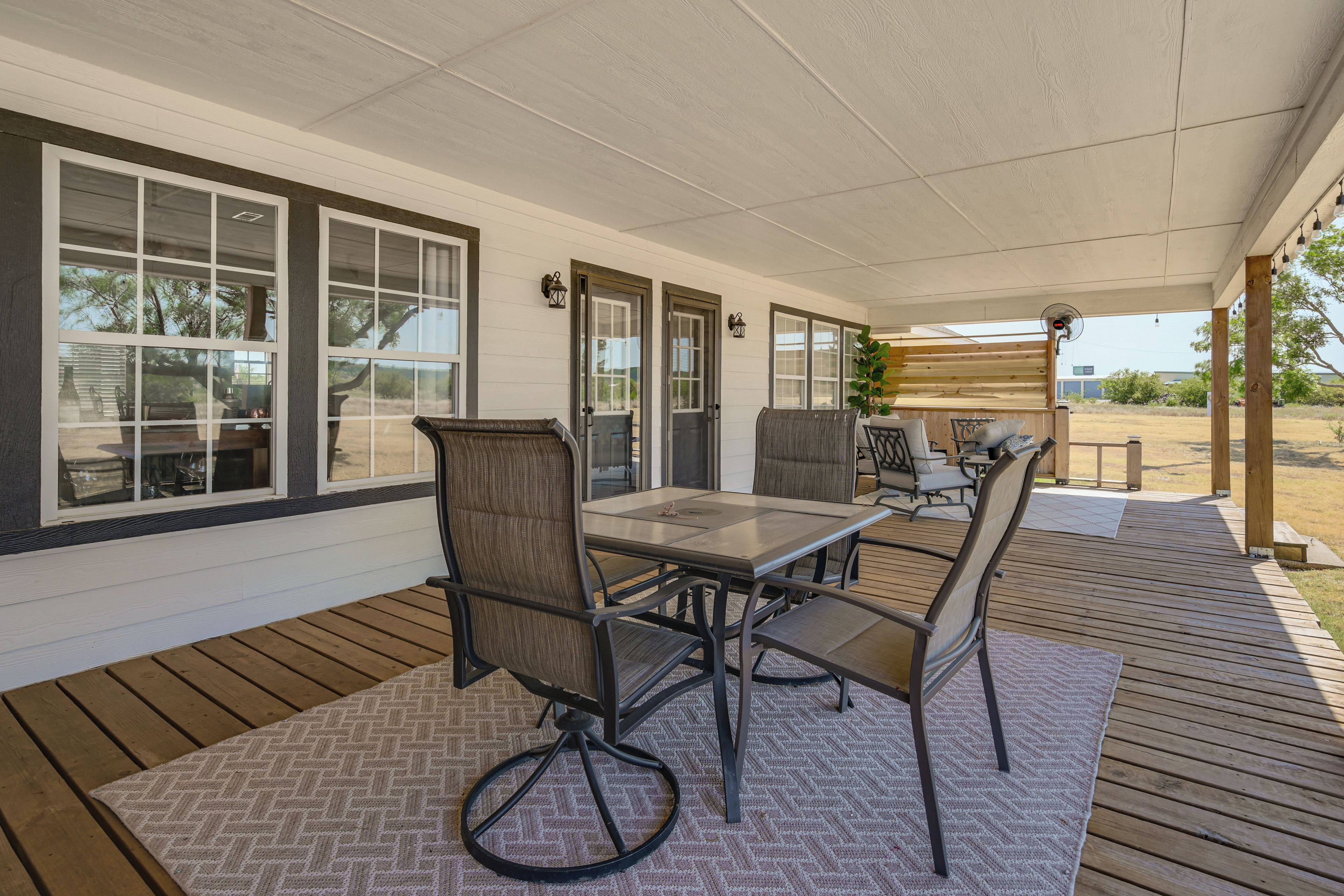 A covered patio area with a table and chairs, large windows, and a wooden deck.
