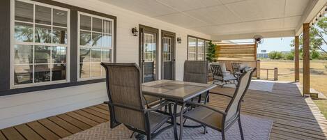A covered patio area with a table and chairs, large windows, and a wooden deck.